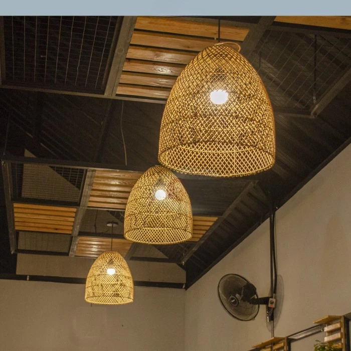 Trois luminaire avec abat-jour en rotin suspendus, on dirait des paniers. Leur câble passe dan sles trou d'un faut plafond décoratif en métal et bois. On voit un ventilateur accroché sur le mur de droite 